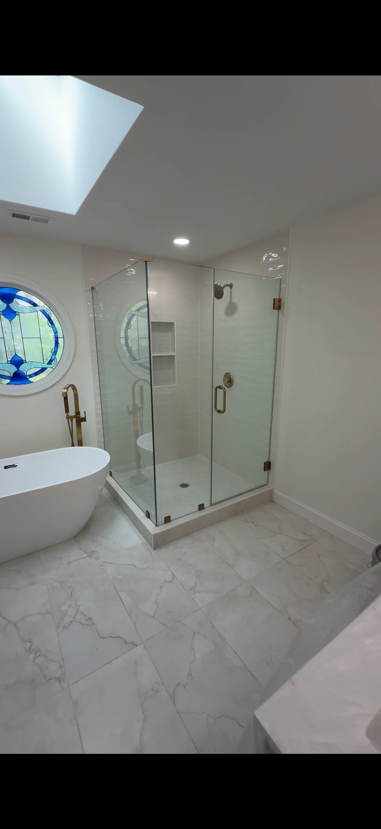 Modern bathroom with frameless glass shower enclosure, white soaking tub, and marble flooring