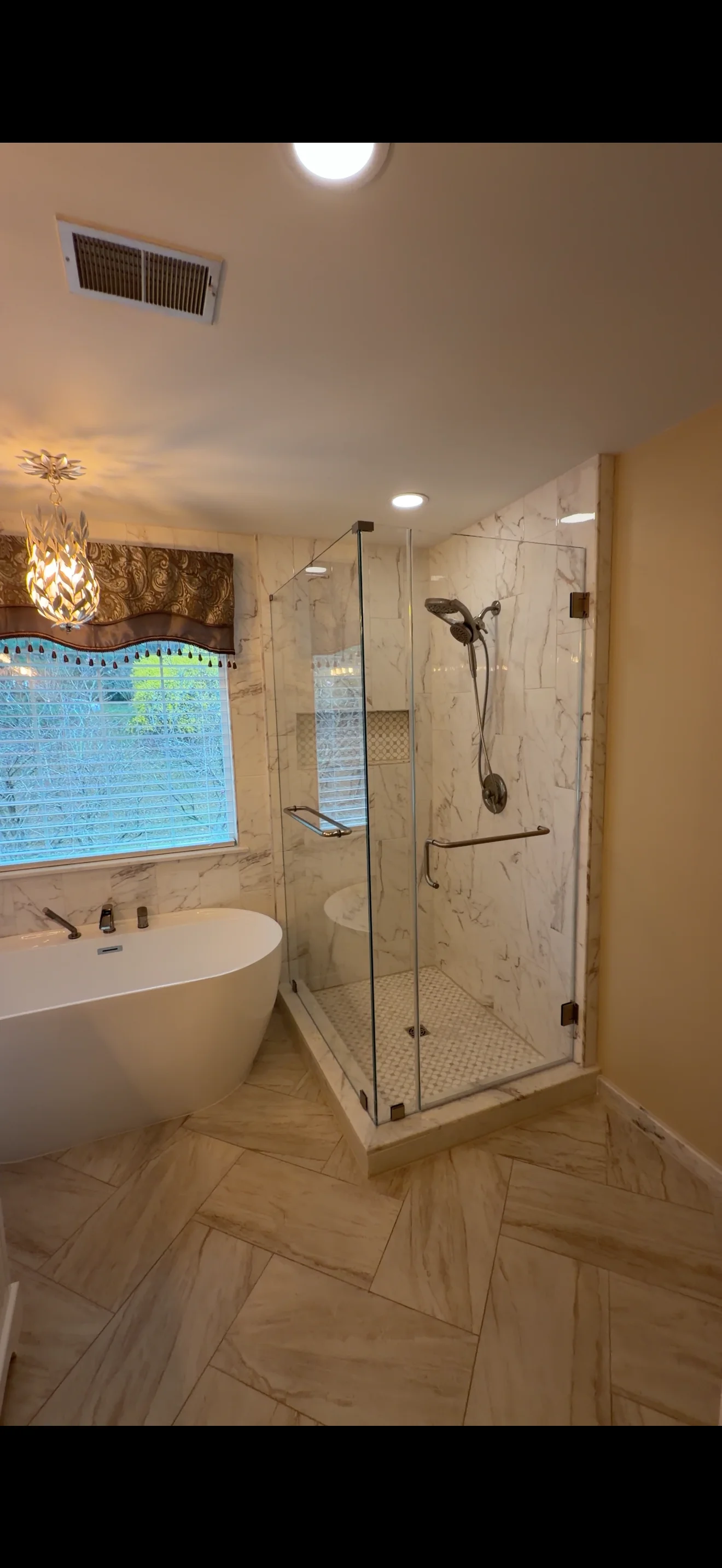 Frameless glass shower enclosure with bronze fixtures in marble-tiled bathroom