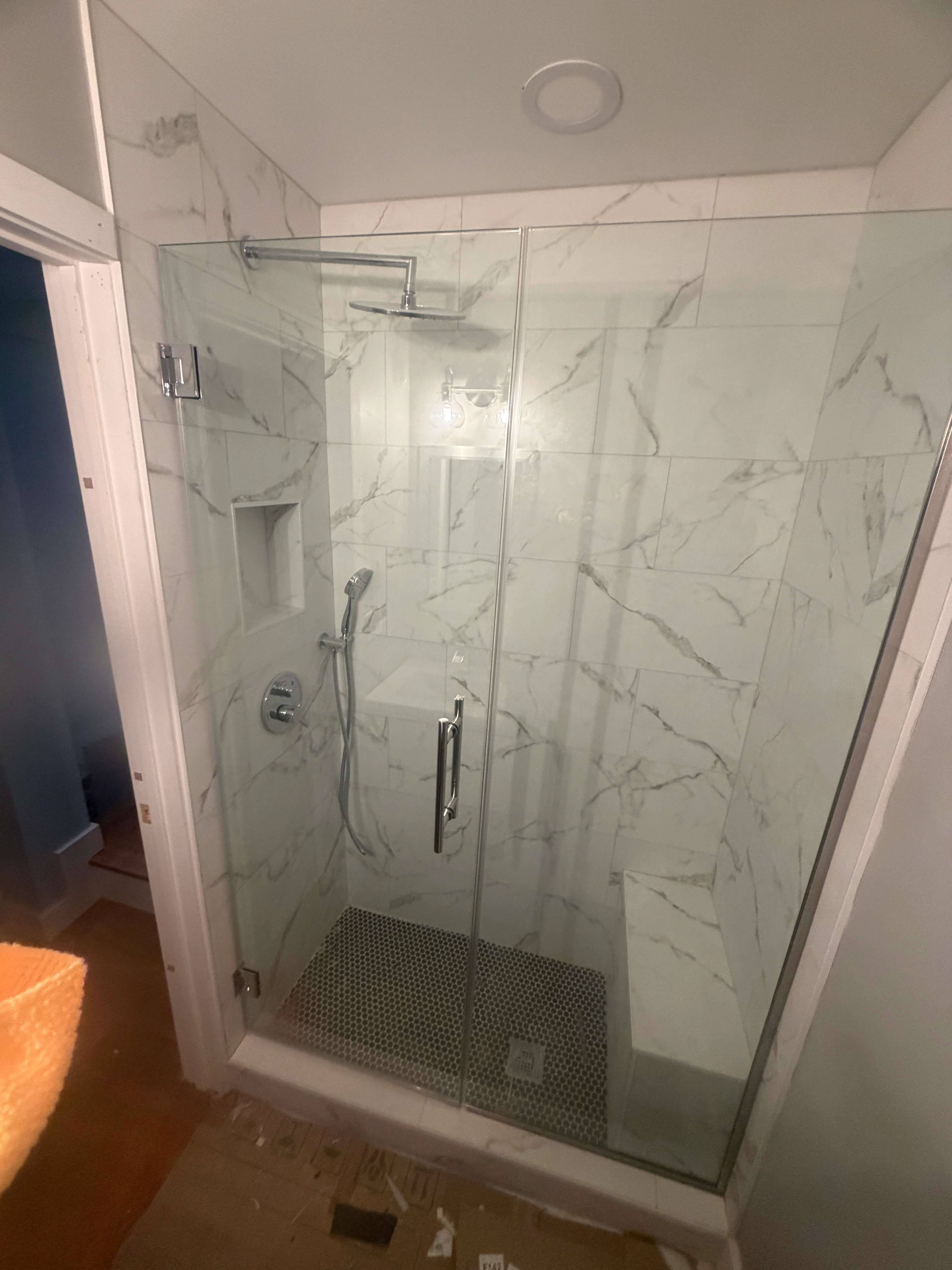 Frameless glass shower enclosure with marble tile walls and hexagonal floor tile in Maryland