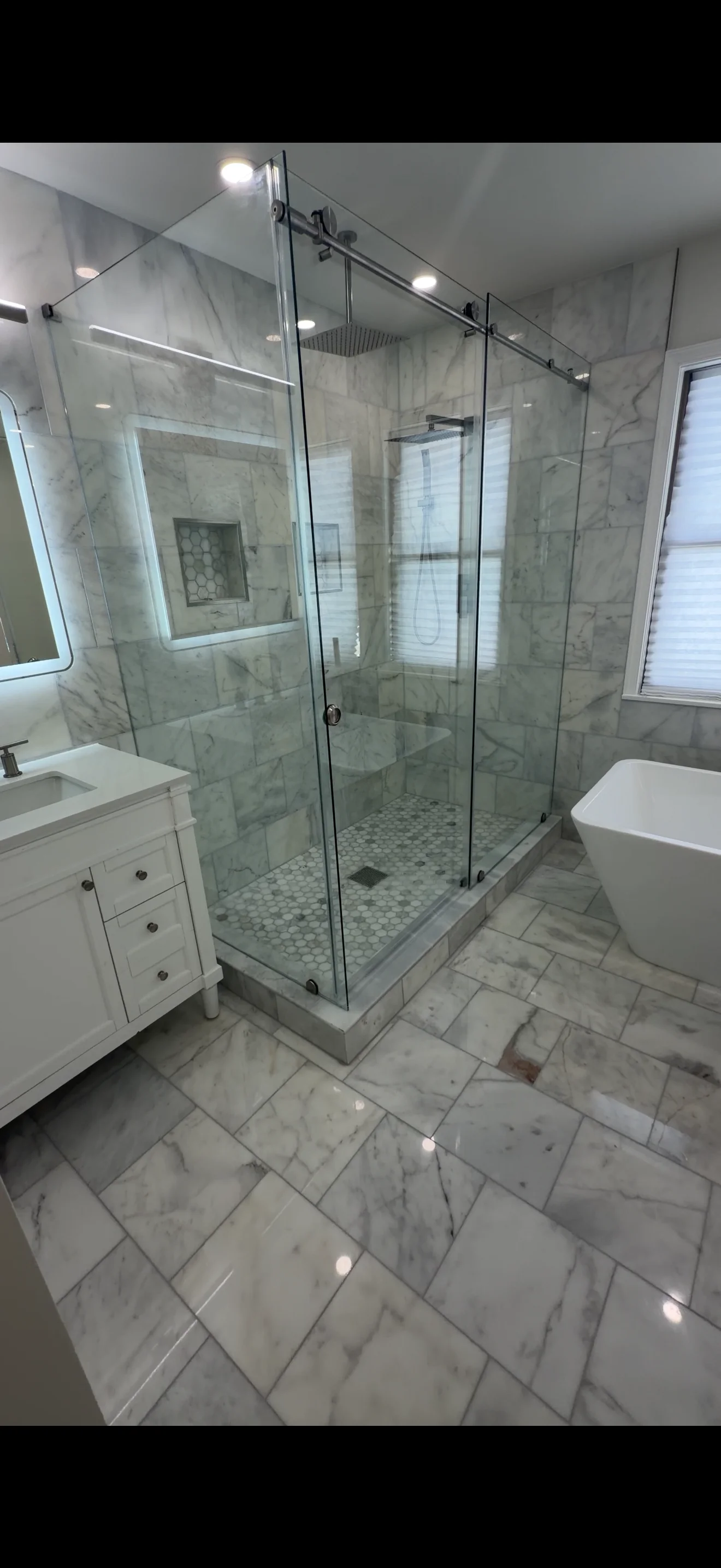 Frameless glass shower enclosure with sliding doors and marble tile surround in modern bathroom