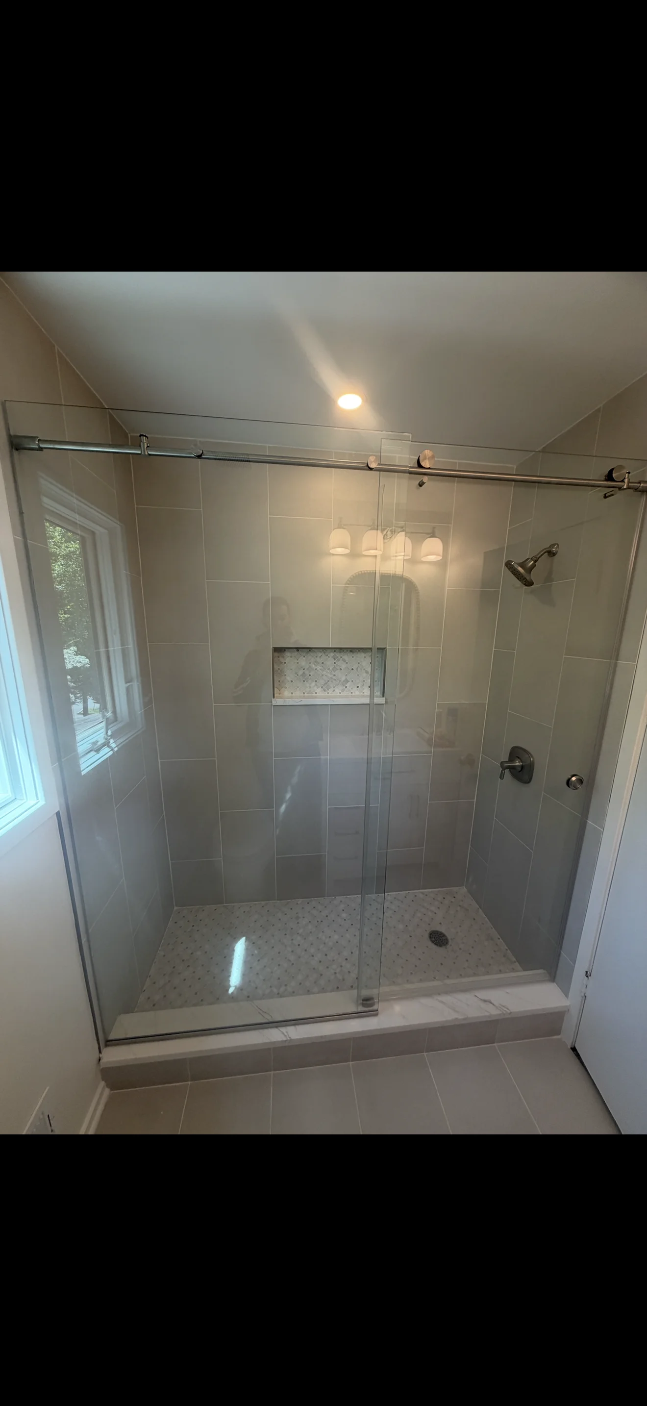 Frameless glass shower enclosure with sliding door and marble tile accents