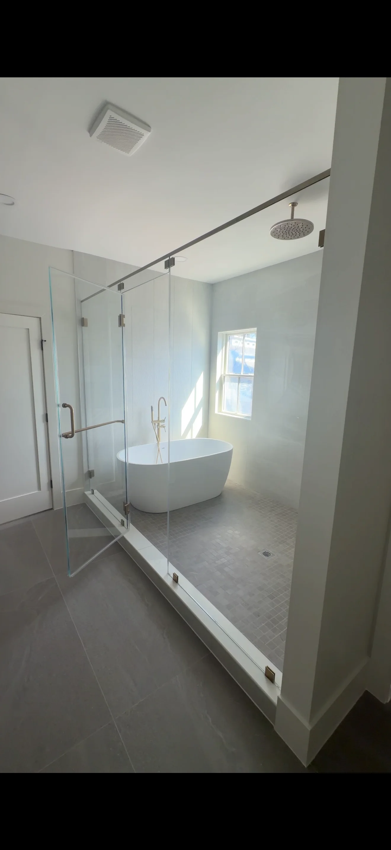 Frameless glass shower enclosure with brushed nickel hinges and freestanding white tub