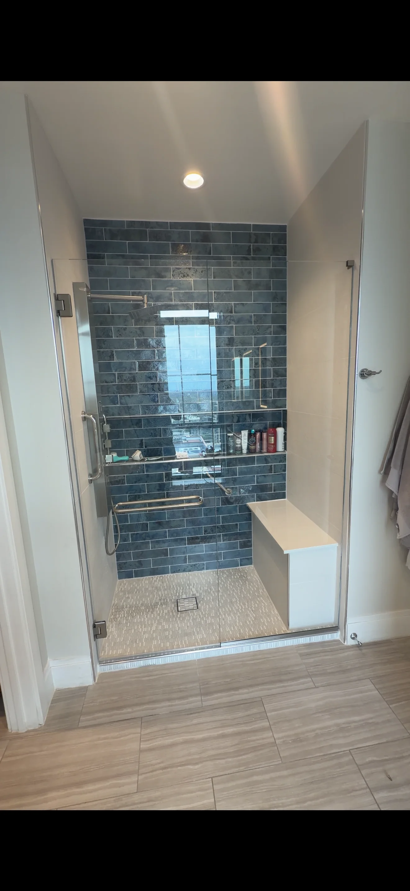Frameless glass shower with dark blue subway tile, built-in bench, and chrome fixtures
