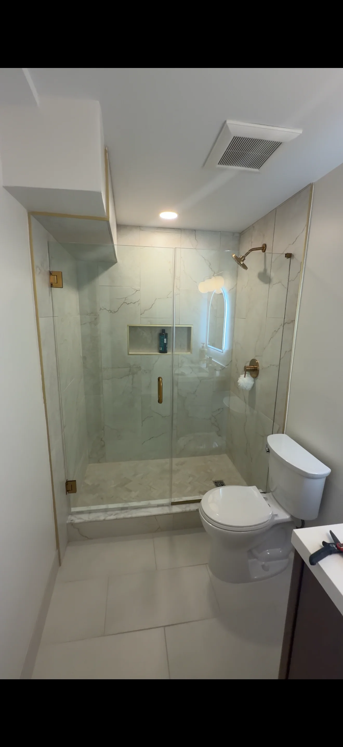 Frameless glass shower enclosure with brushed gold hardware and marble tile surround in modern bathroom