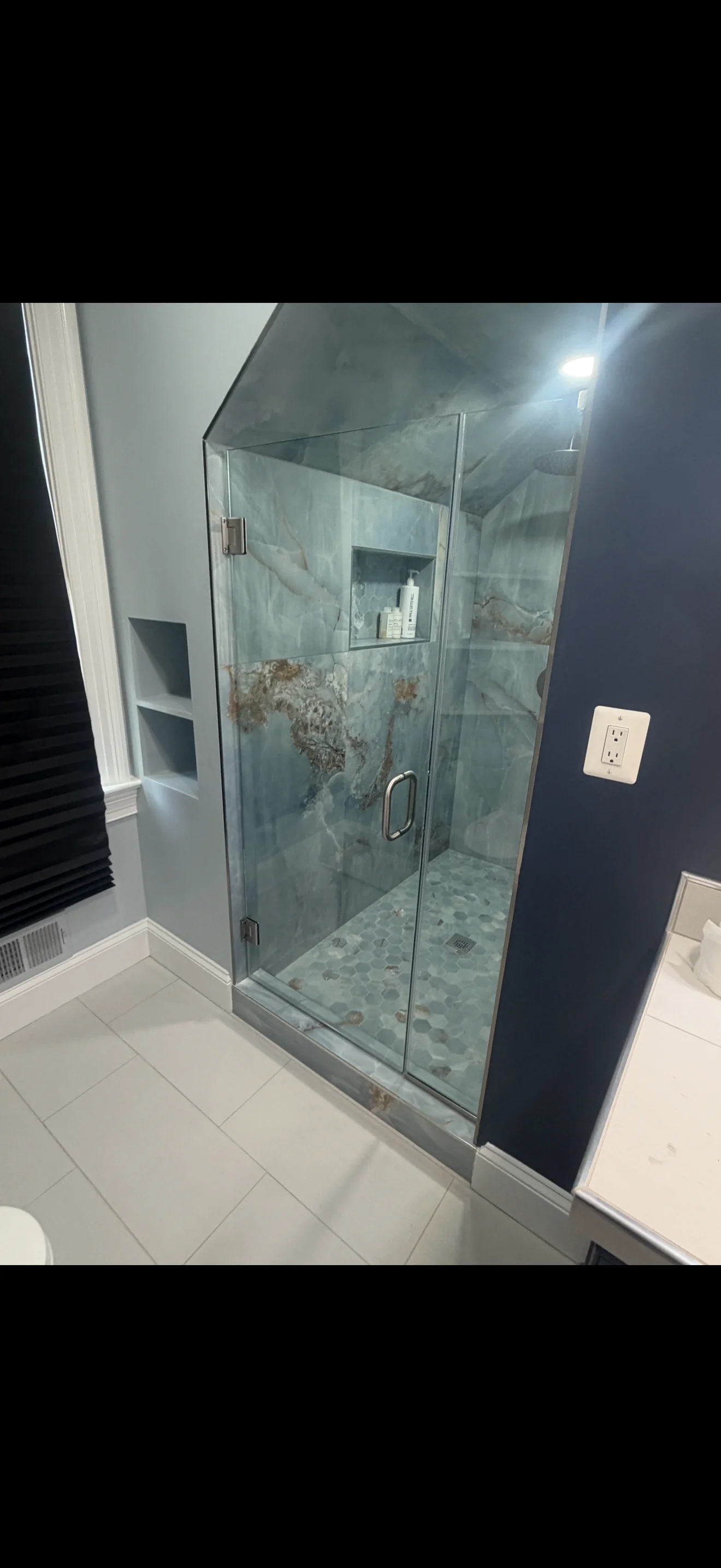 Frameless glass shower enclosure with marble-look tile and chrome hardware in modern bathroom