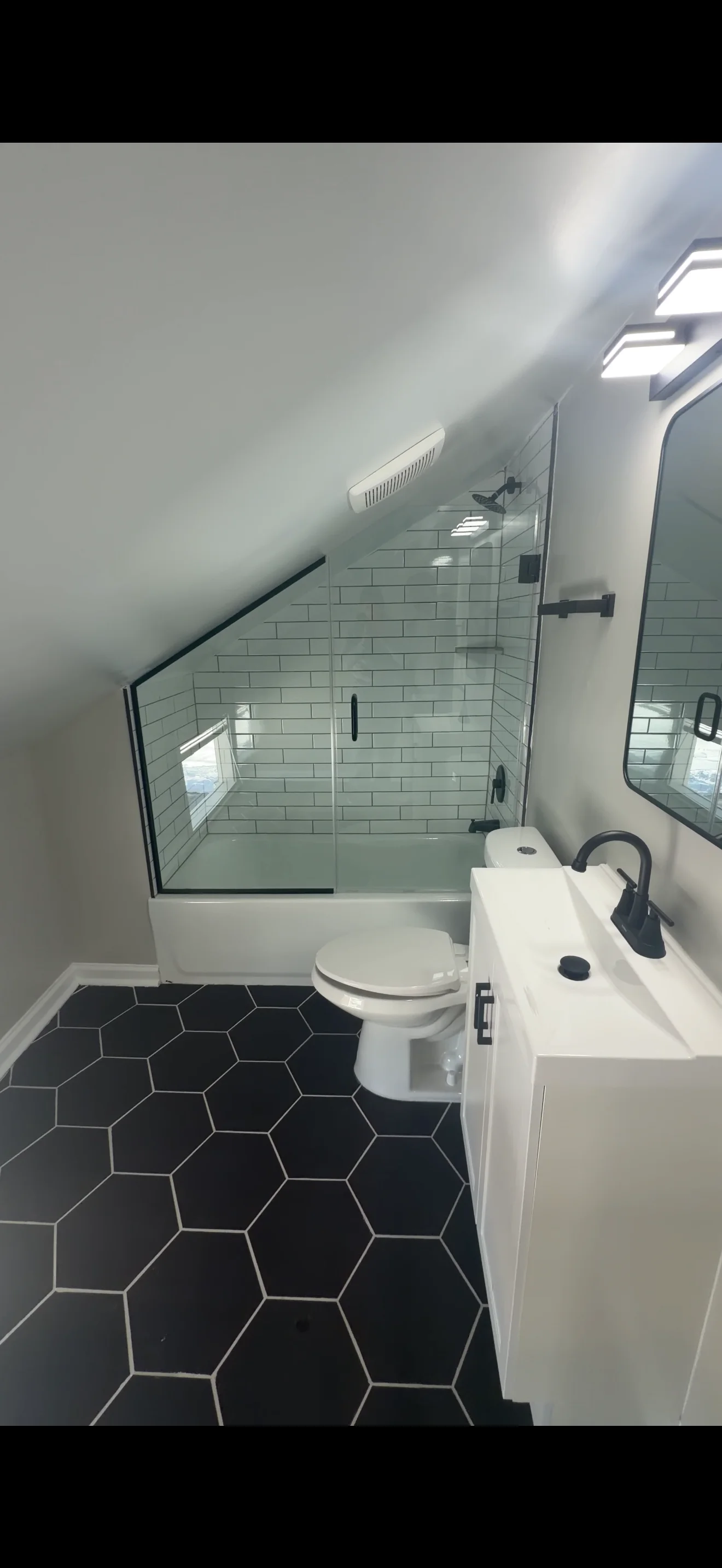 Frameless glass shower enclosure with black hardware in modern bathroom with hexagonal tile floor