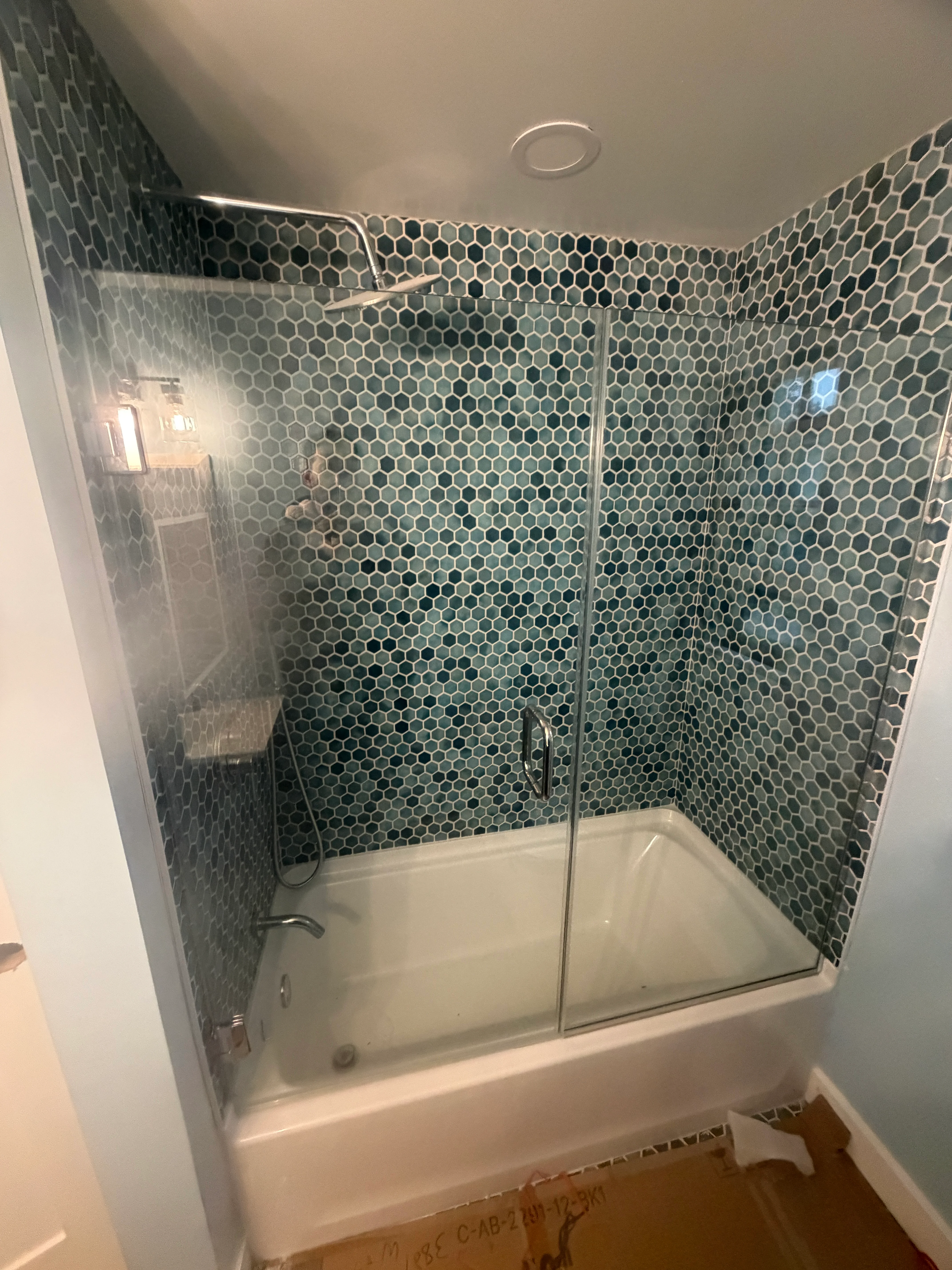 Frameless glass shower enclosure with hexagonal tile walls and chrome hardware