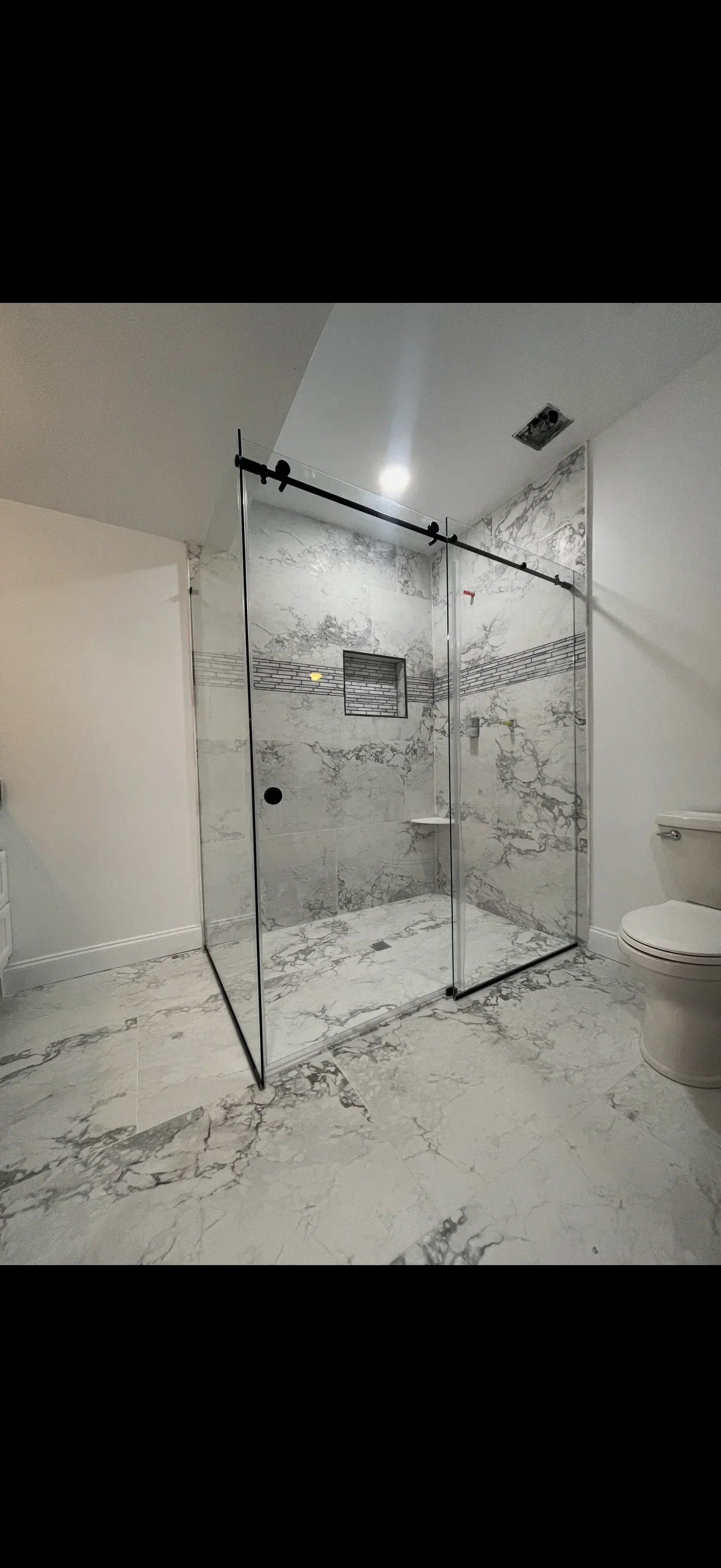 Frameless glass shower enclosure with black hardware and marble tile surround in modern bathroom