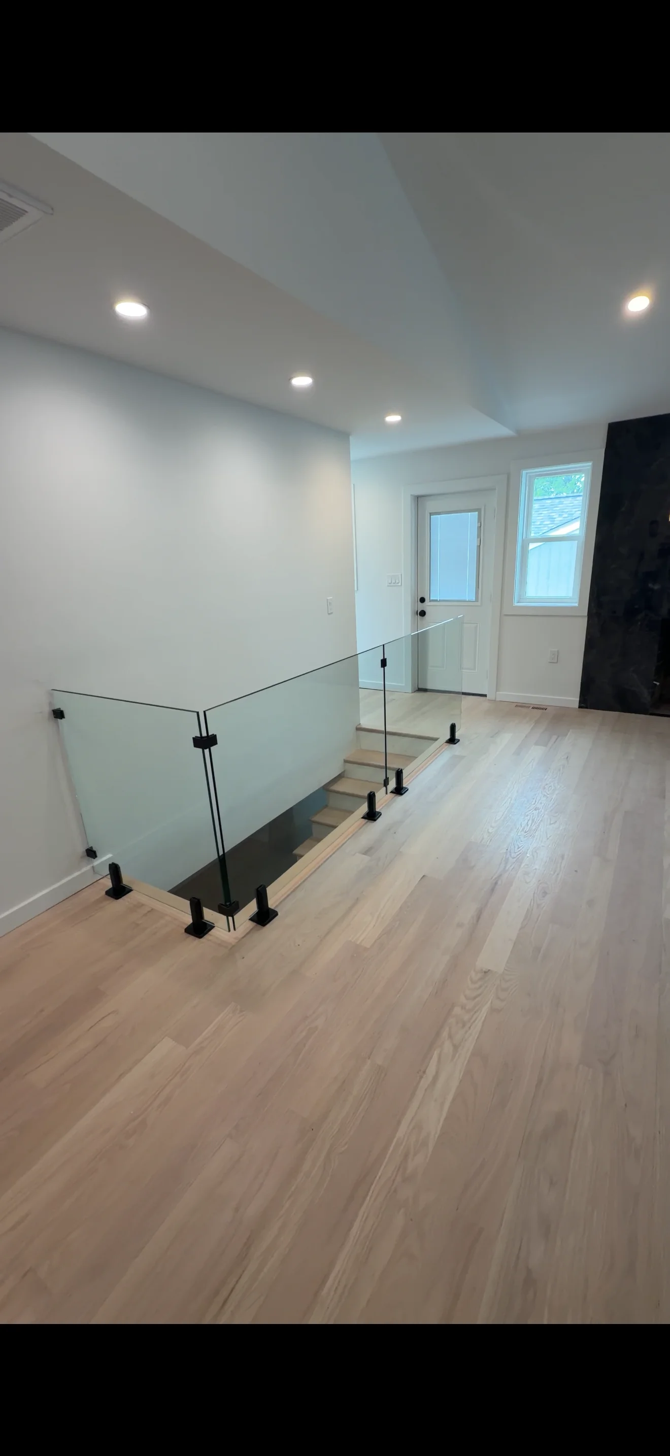Frameless glass railing with black metal posts along residential staircase