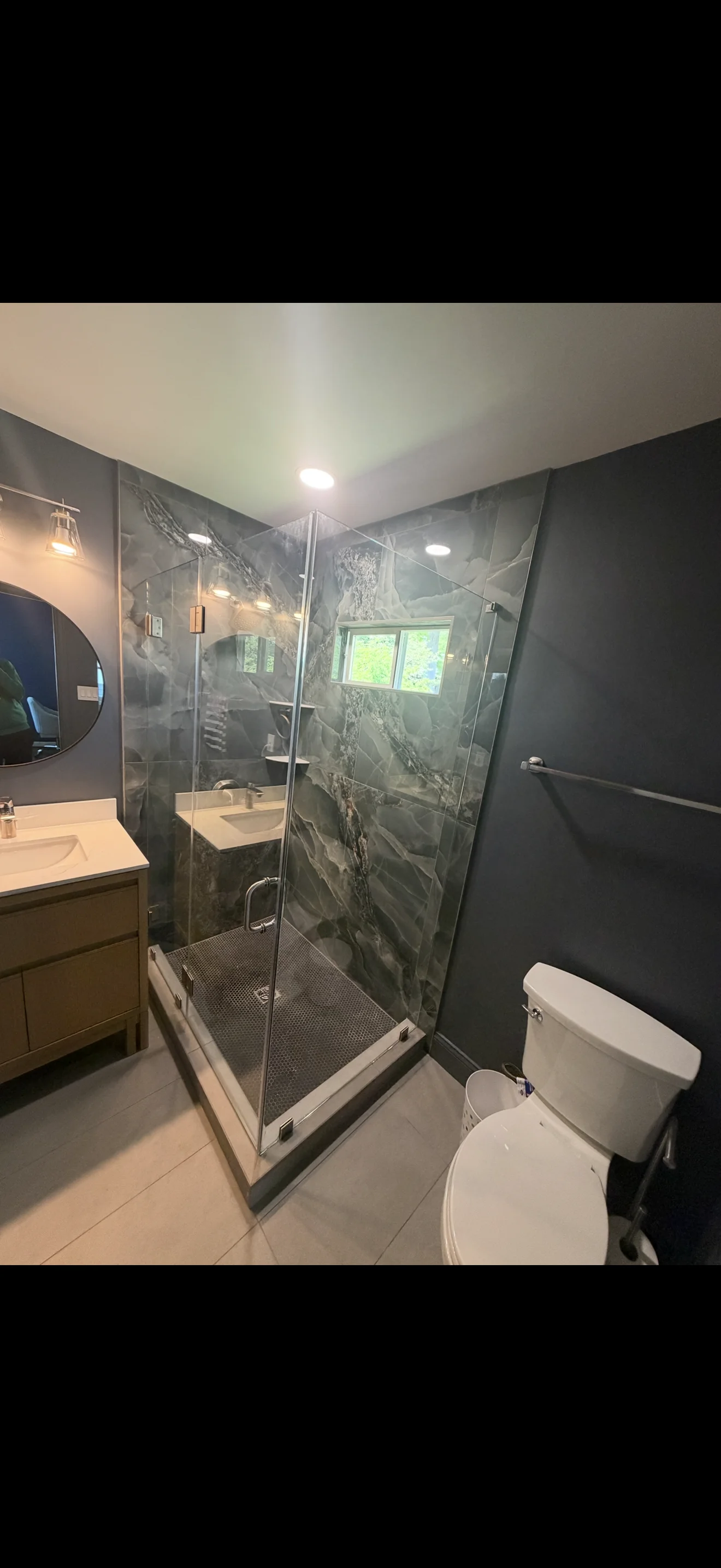 Frameless glass shower enclosure with marble tile and chrome fixtures in modern bathroom