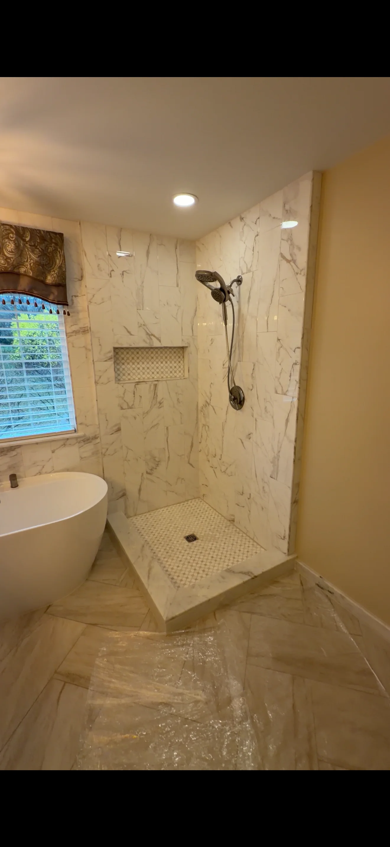 Frameless glass shower enclosure with marble tile walls and bronze fixtures in modern bathroom