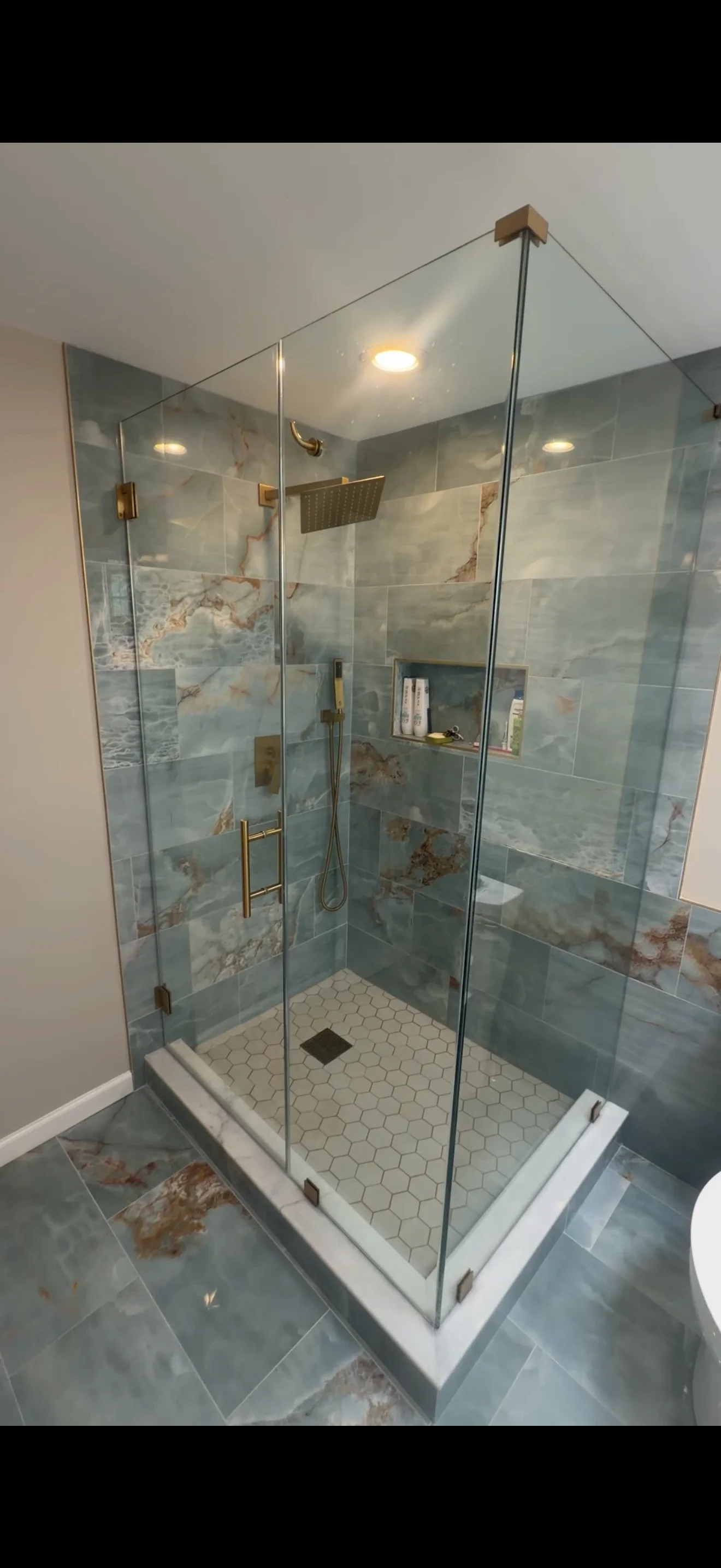 Frameless glass shower enclosure with marble tile and brass hardware in modern bathroom