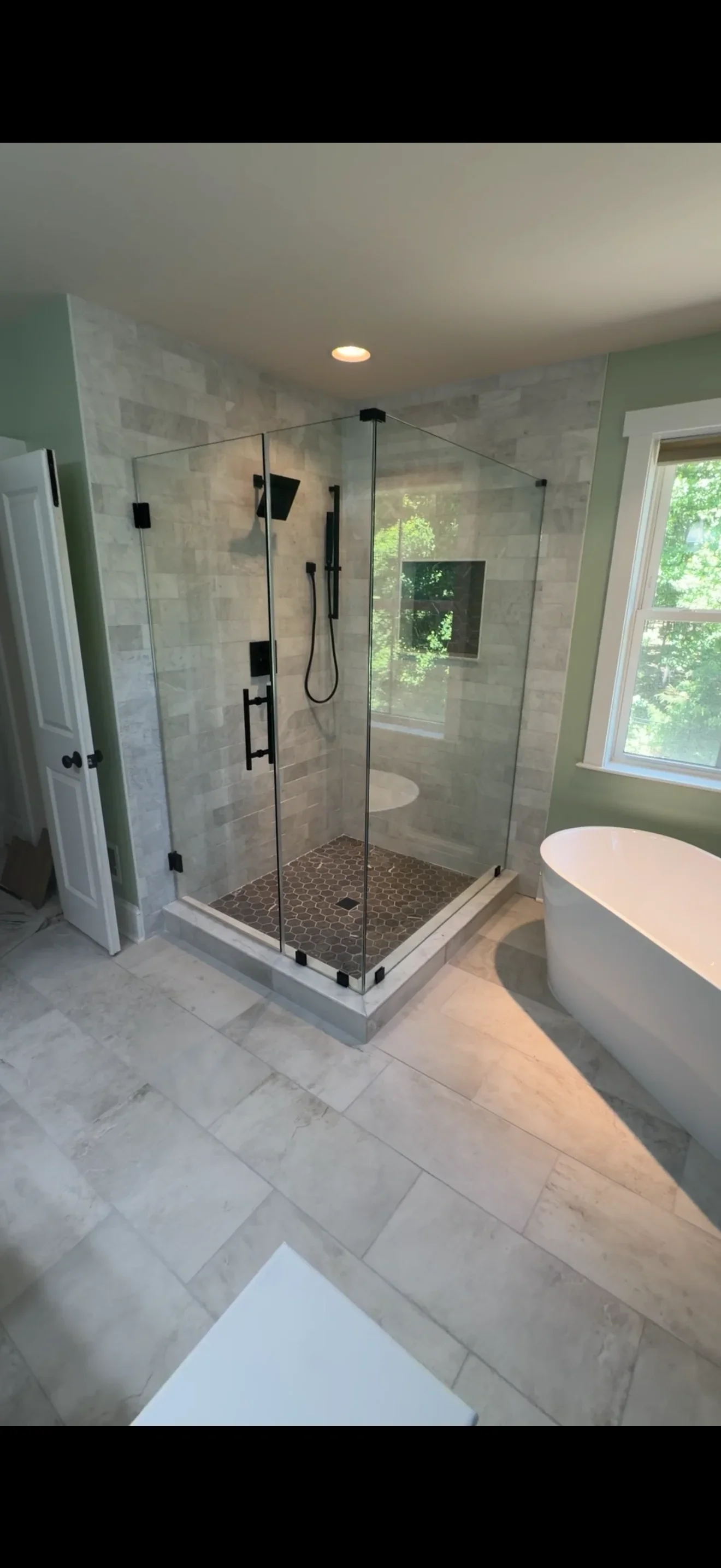 Frameless glass shower enclosure with black hardware and pebble floor in modern bathroom